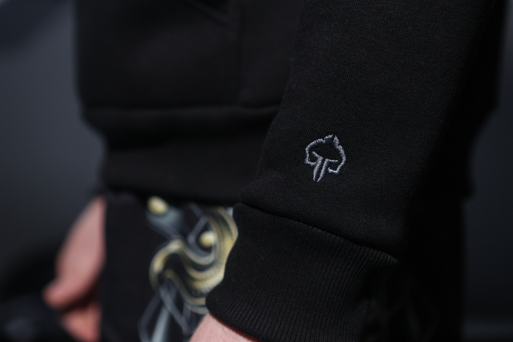 Close-up of black hoodie sleeve cuff with small embroidered tree logo detail.