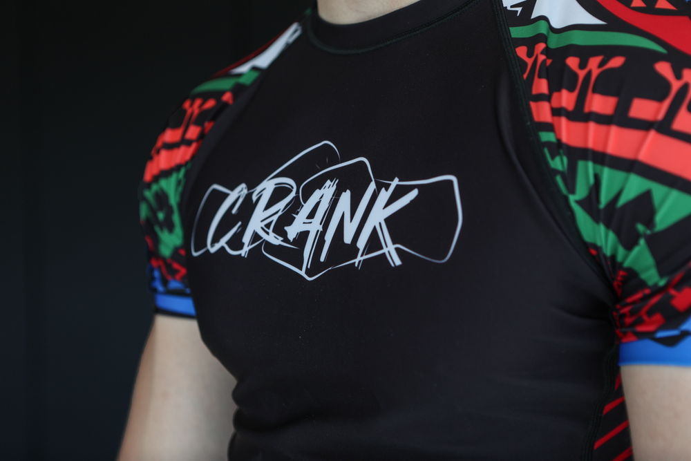 Person wearing a black CRANK branded rashguard with colorful geometric pattern sleeves.