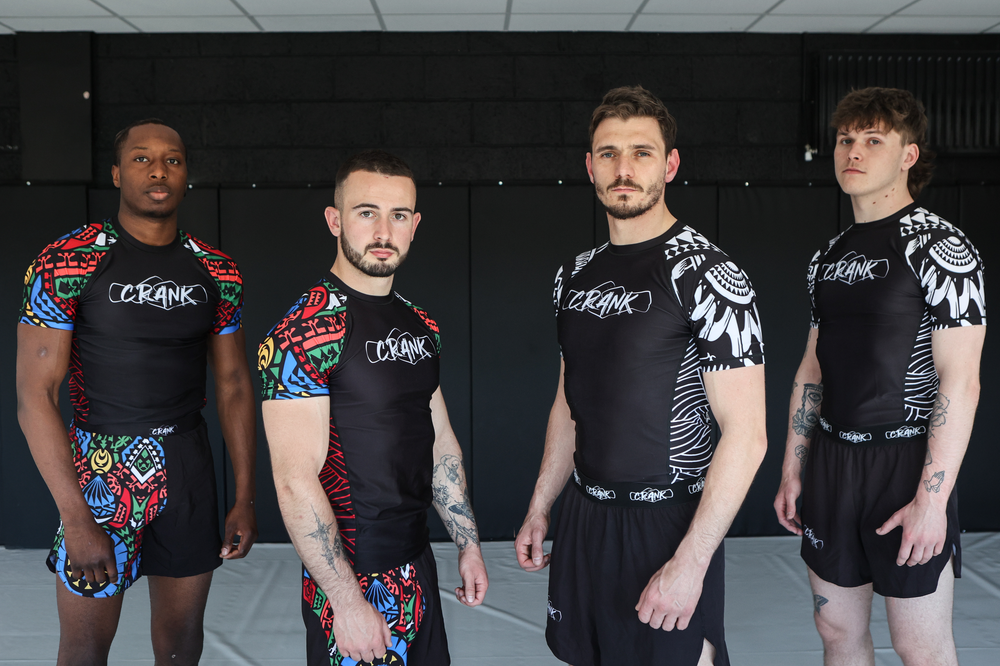 Four male MMA athletes posing in colorful Crank branded rashguards against dark background.