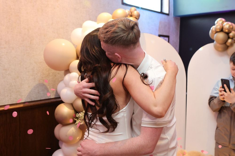 Couple sharing a romantic wedding kiss embrace surrounded by gold and cream balloon arch decorations.