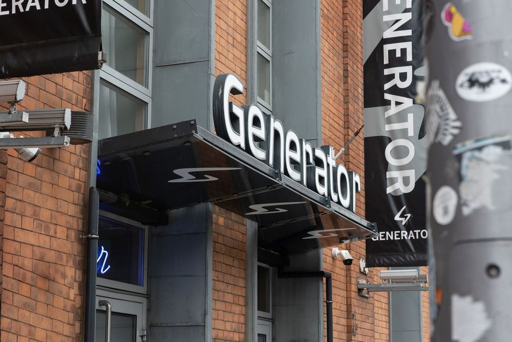 Exterior brick facade of Generator hostel with illuminated signage in urban setting.