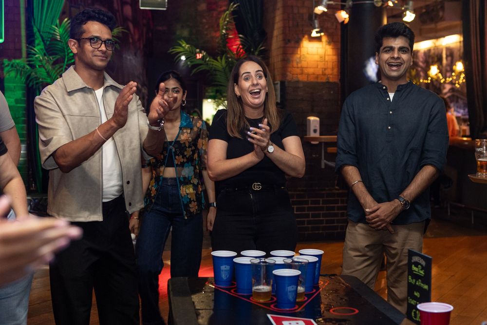 Group of friends laughing and playing beer pong at a colorful indoor party venue.