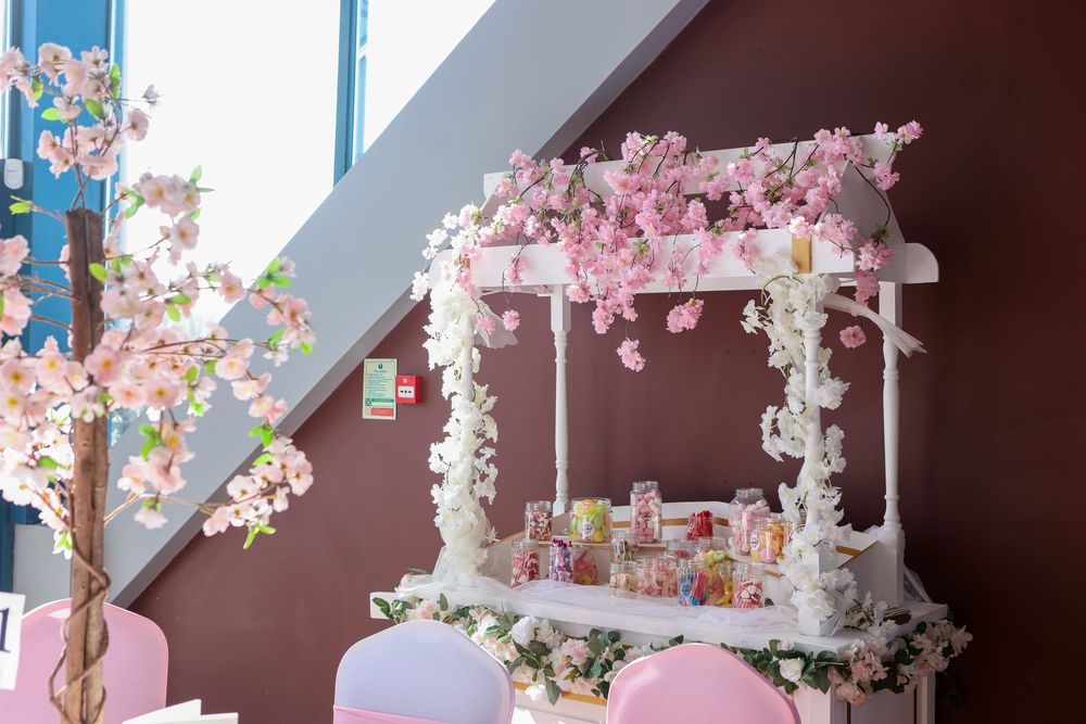 White gazebo decorated with pink cherry blossoms and floral arrangements at an elegant event venue.