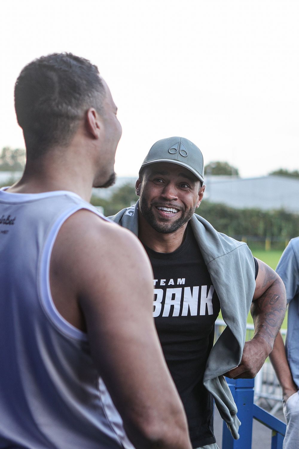 Two athletes in Team Bank shirts chat and smile outdoors after a workout session.