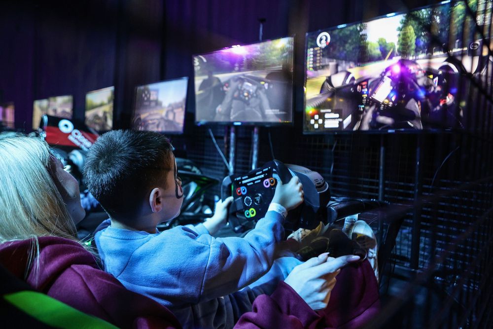 Children playing racing video games with steering wheel controllers at a gaming event.