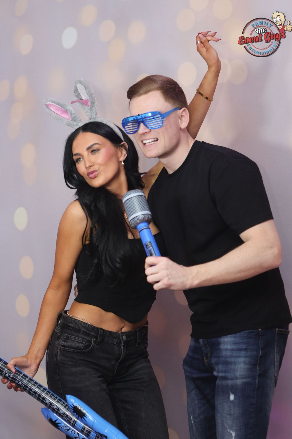 A couple poses playfully at a photo booth, woman wearing bunny ears and man holding a toy microphone.