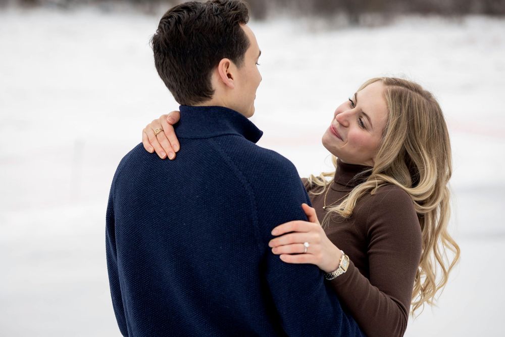 Couple embracing outdoors in winter, woman smiling up at man wearing navy coat, snowy background.