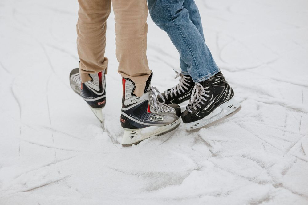 Two people wearing ice skates stand close together on a frozen ice rink surface.