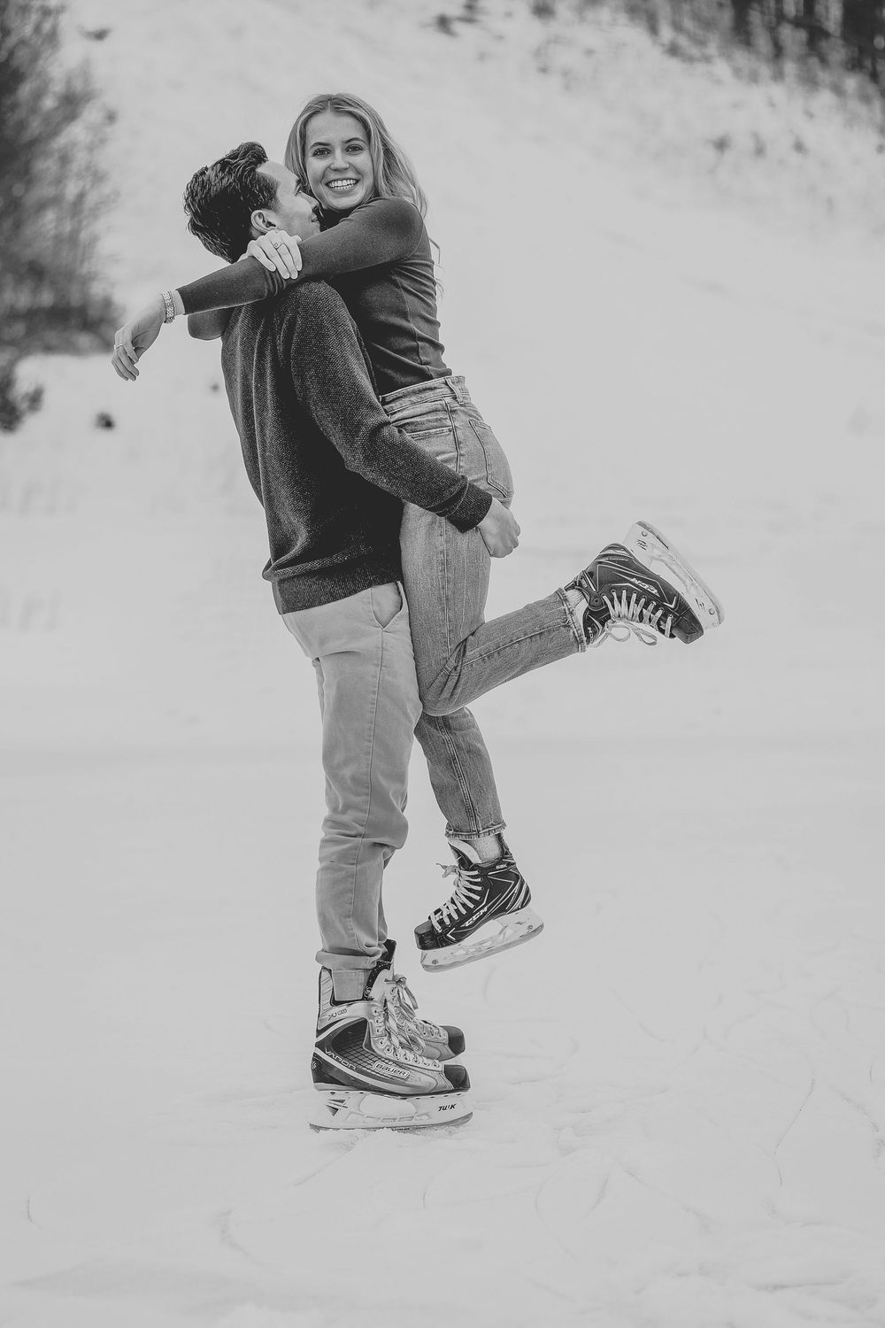 Black and white photo of a couple ice skating, man lifting smiling woman in a joyful winter embrace outdoors.