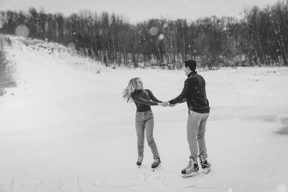 Couple holding hands ice skating on frozen outdoor pond in winter snow, black and white romantic photo.