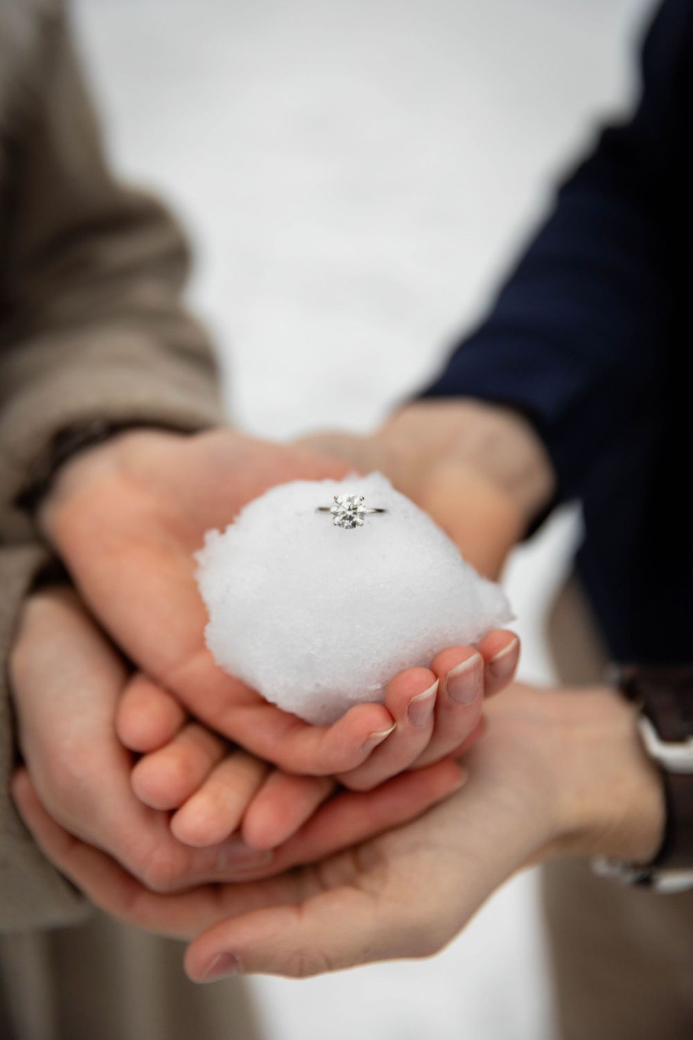 Two people cupping their hands together holding a snowball with a silver snowflake charm on top.