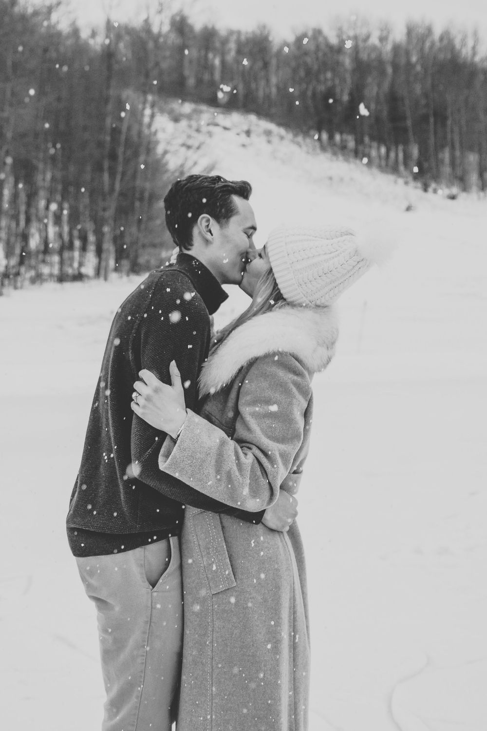 A couple sharing a romantic kiss in a snowy winter landscape, with snowflakes falling around them.