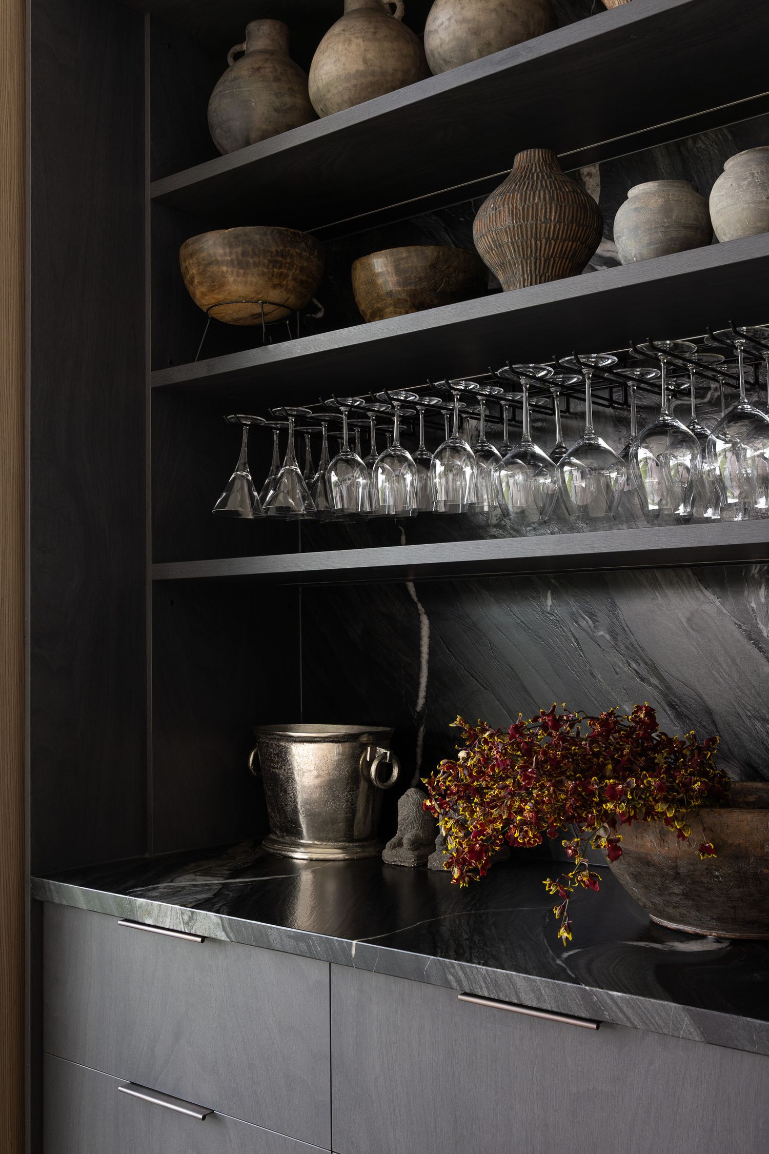 Dark shelving unit with wine glasses, ceramic vases, bowls, and autumn floral arrangement on marble countertop.