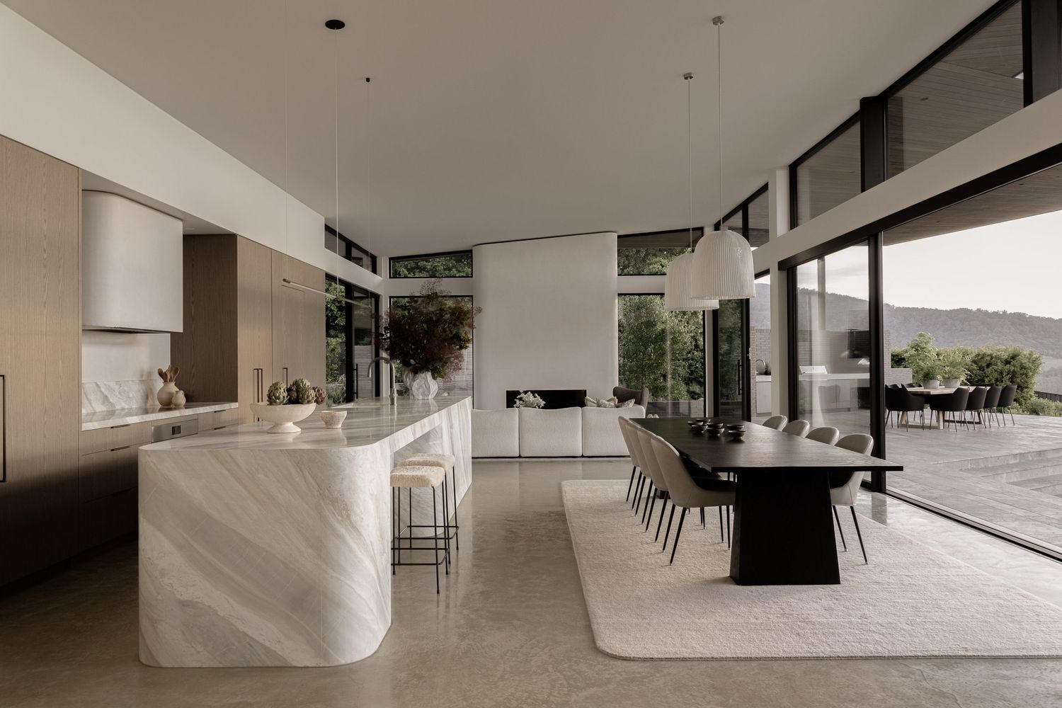 Modern open-plan kitchen and dining area featuring marble island, black dining table, and floor-to-ceiling windows with outdoor views.