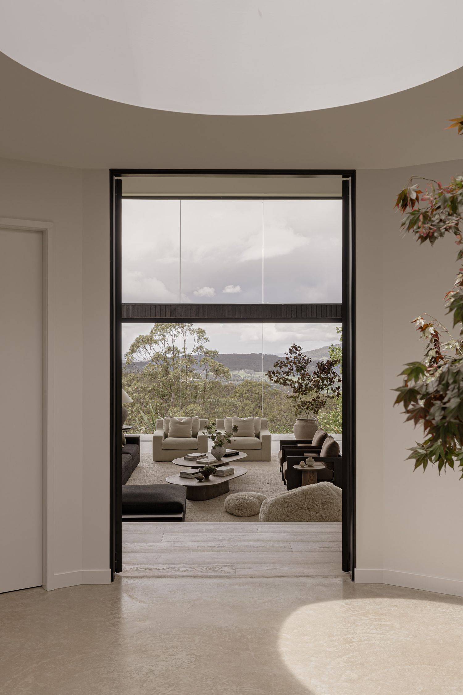 Modern interior doorway framing an outdoor living area with neutral furniture and panoramic tree-lined views.