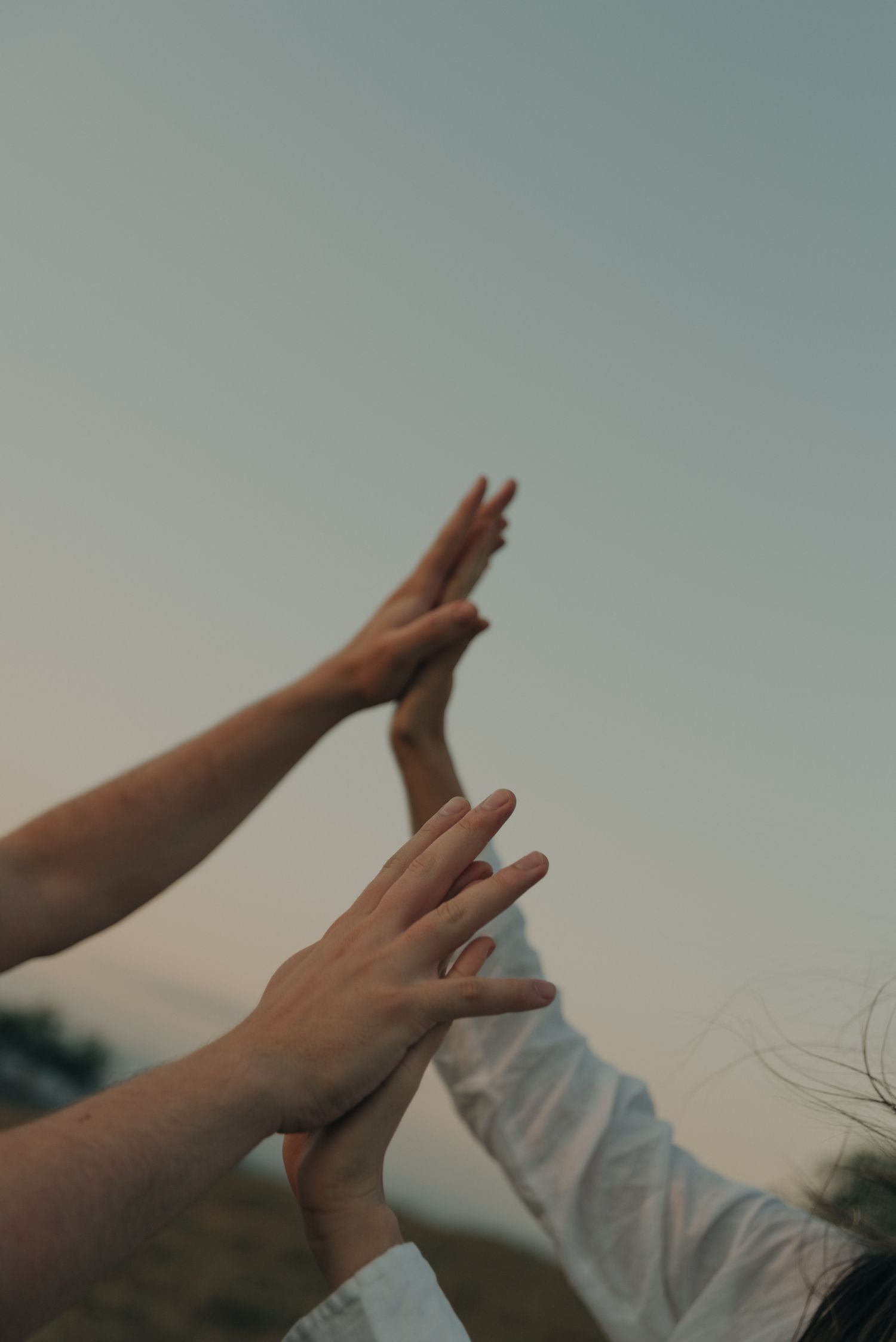 Multiple hands reaching up to touch in a high-five gesture against a dusky sky.