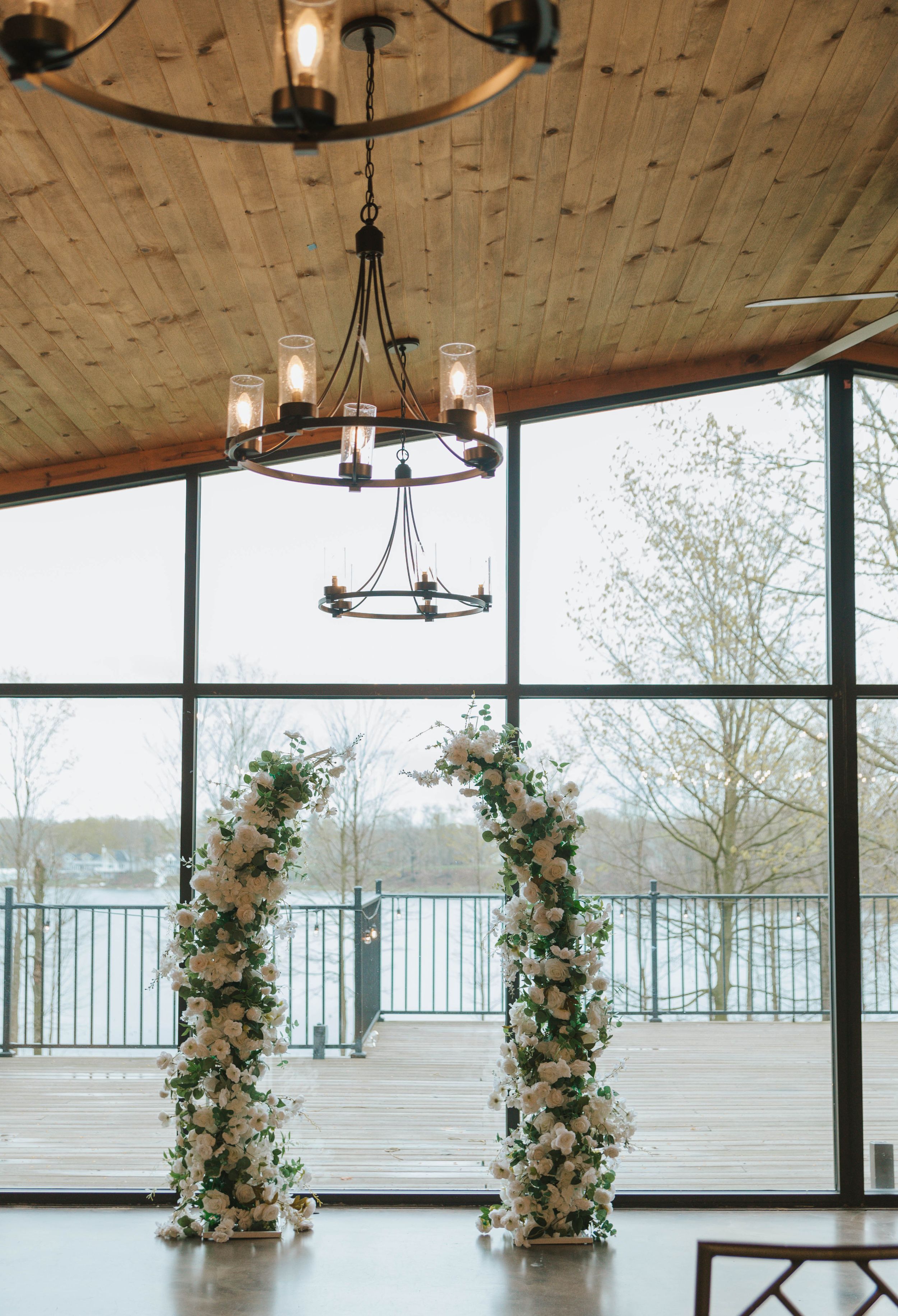 Elegant wedding arch adorned with white and blush florals in a lakeside venue with wood ceiling and chandelier.