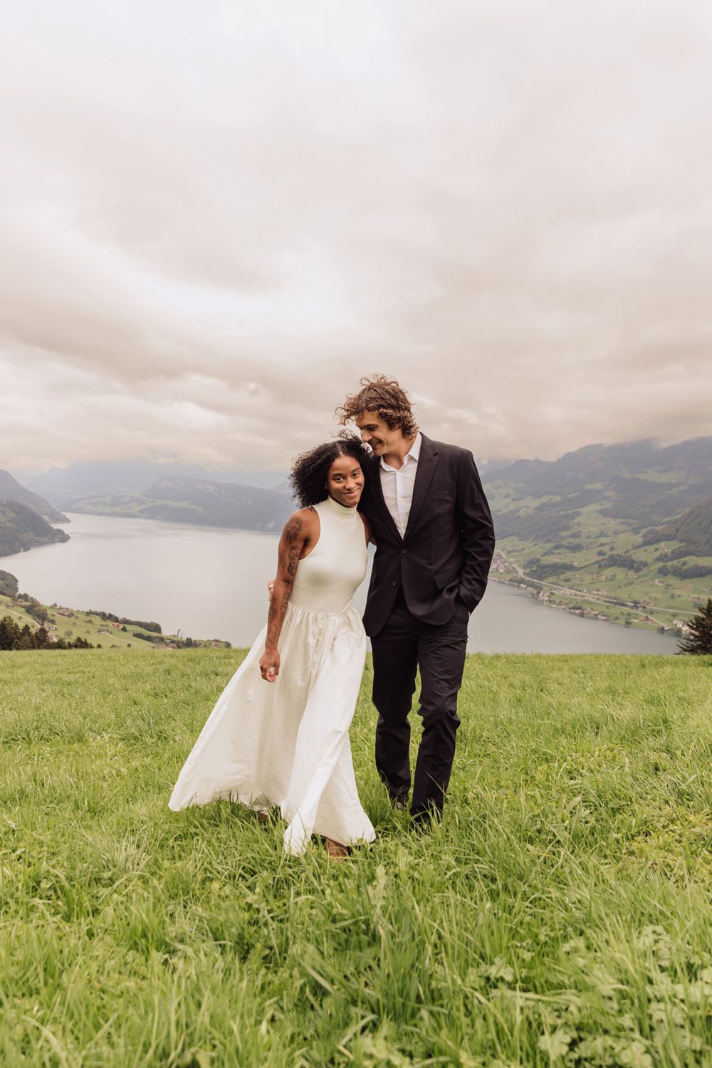 Romantic portrait of a couple embracing on a scenic mountain ridge under a soft, overcast sky.