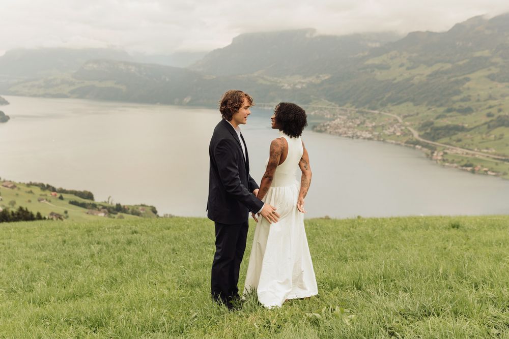 Cinematic landscape photo of a couple holding hands in a vast green field by a mountain in Switzerland