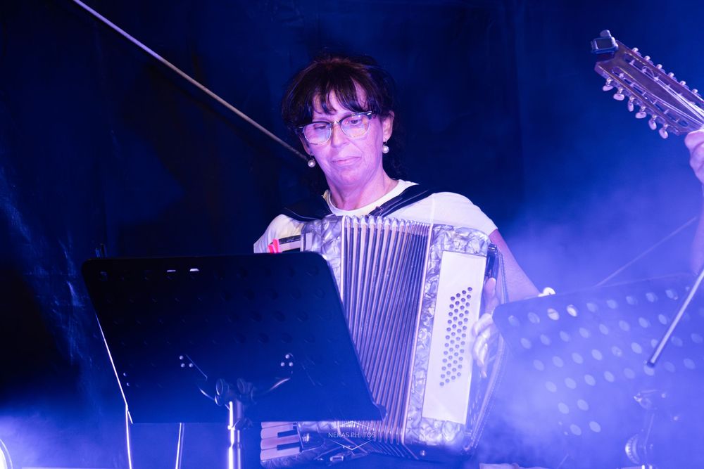 Woman playing accordion on stage under blue lights at a live music performance.