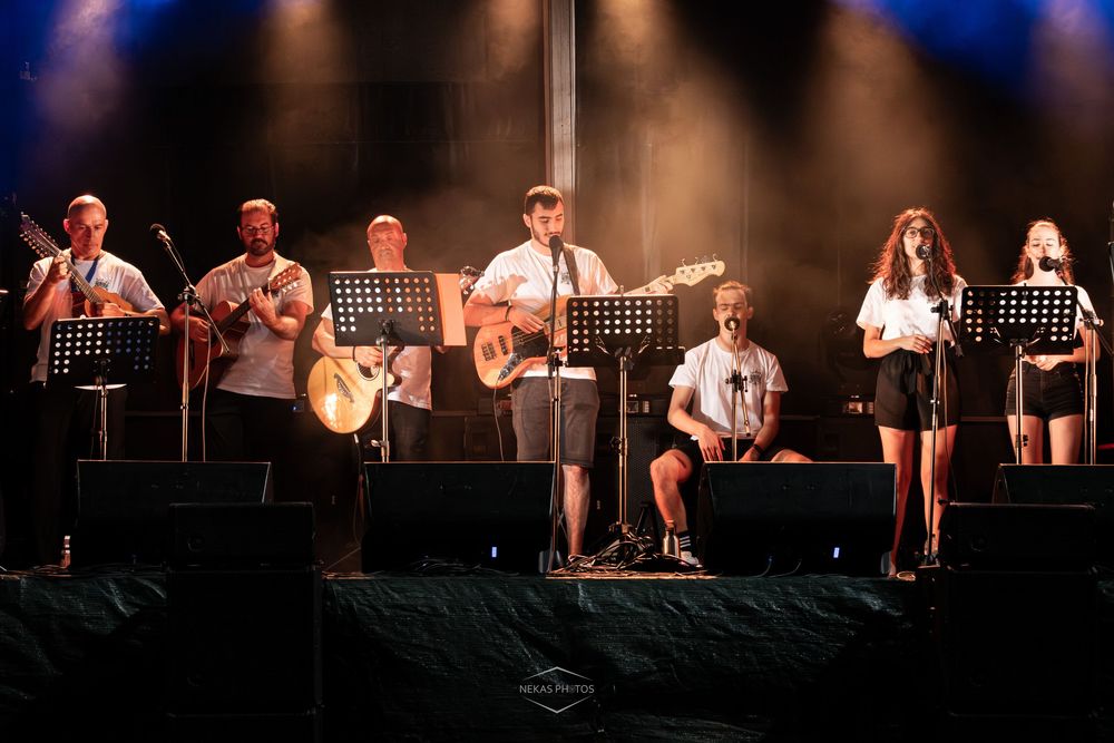 Band performing on stage at outdoor music festival with guitars, microphones, and music stands under dramatic lighting.