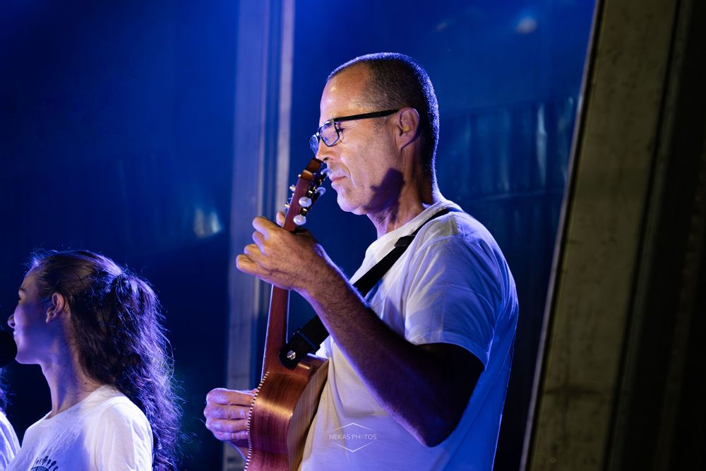 Man in white shirt playing guitar on stage under blue lights during a live music performance.