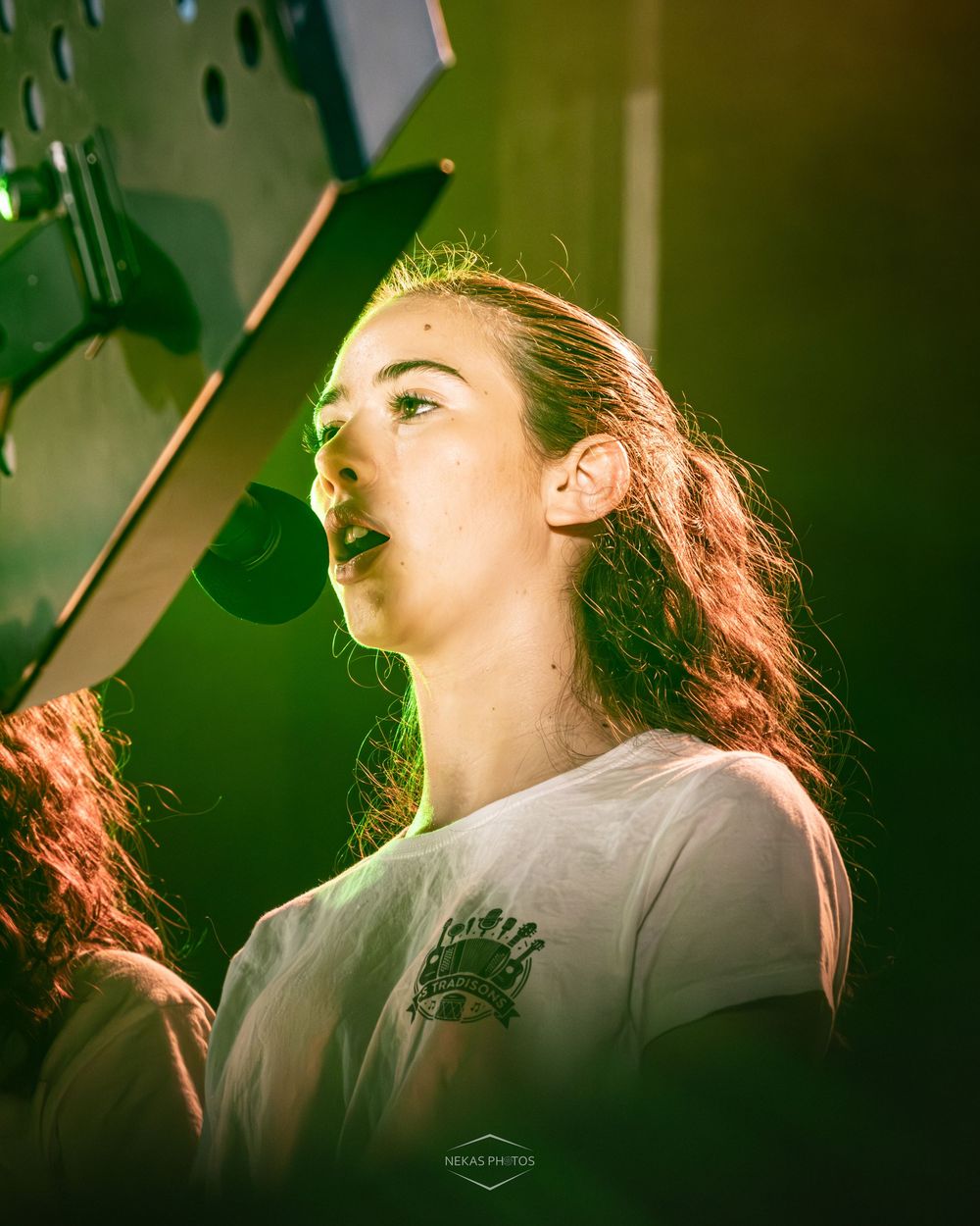 Young woman with long hair performing on stage under dramatic green and yellow concert lighting.