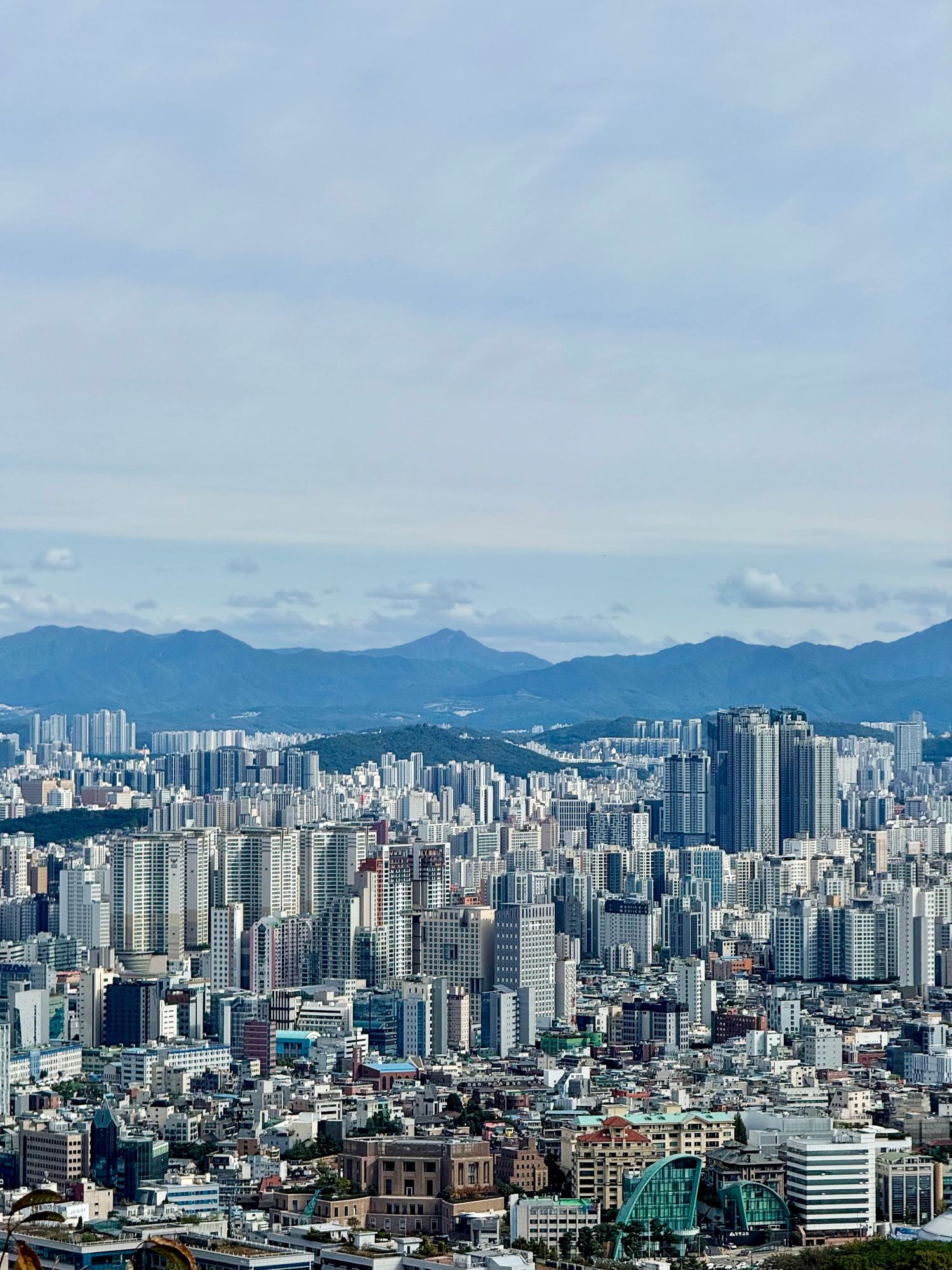 Aerial panoramic view of dense Seoul cityscape with skyscrapers and mountains in background, South Korea.