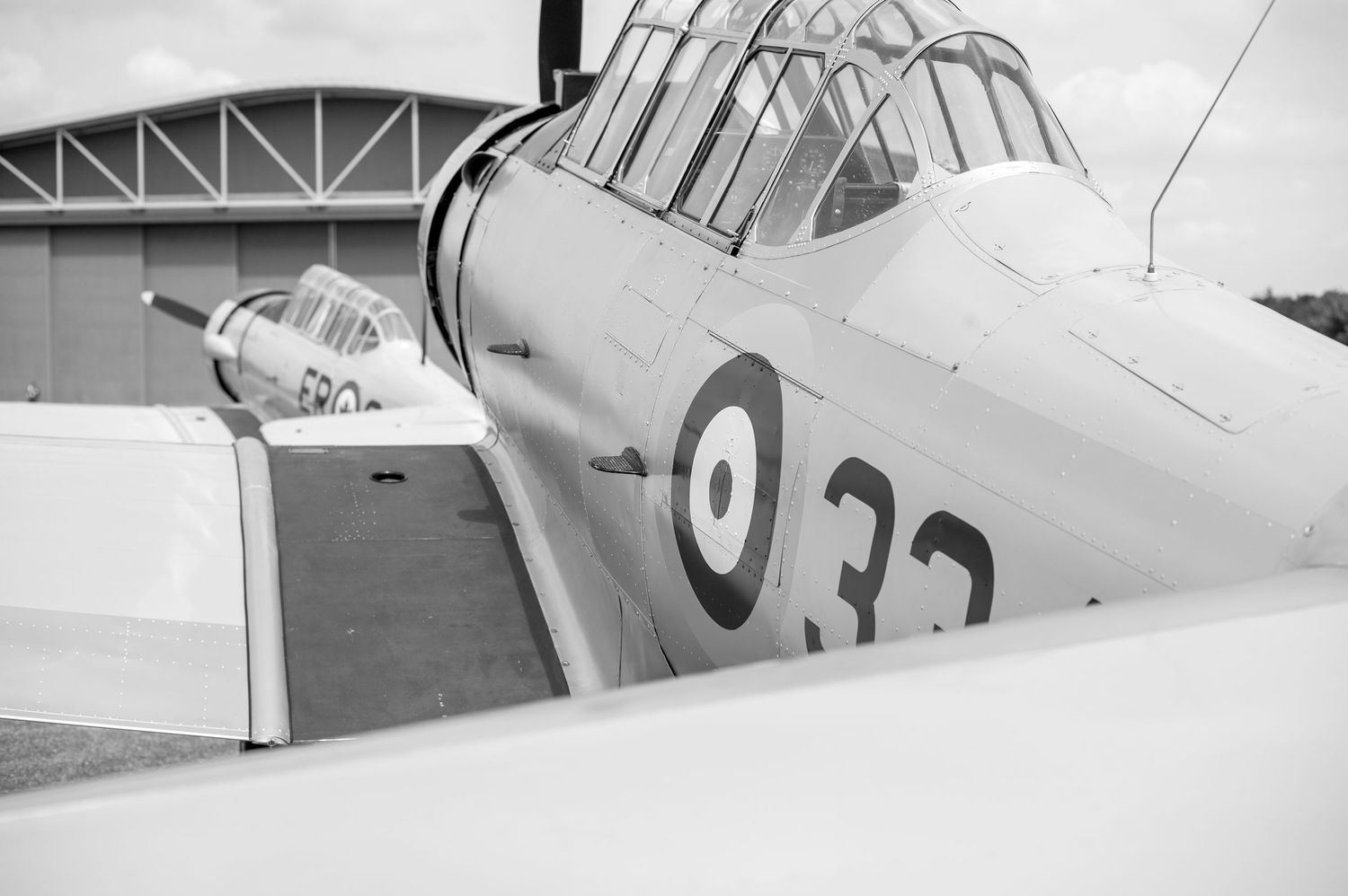 Black and white photo of a vintage military propeller aircraft with roundel markings, parked near a hangar.