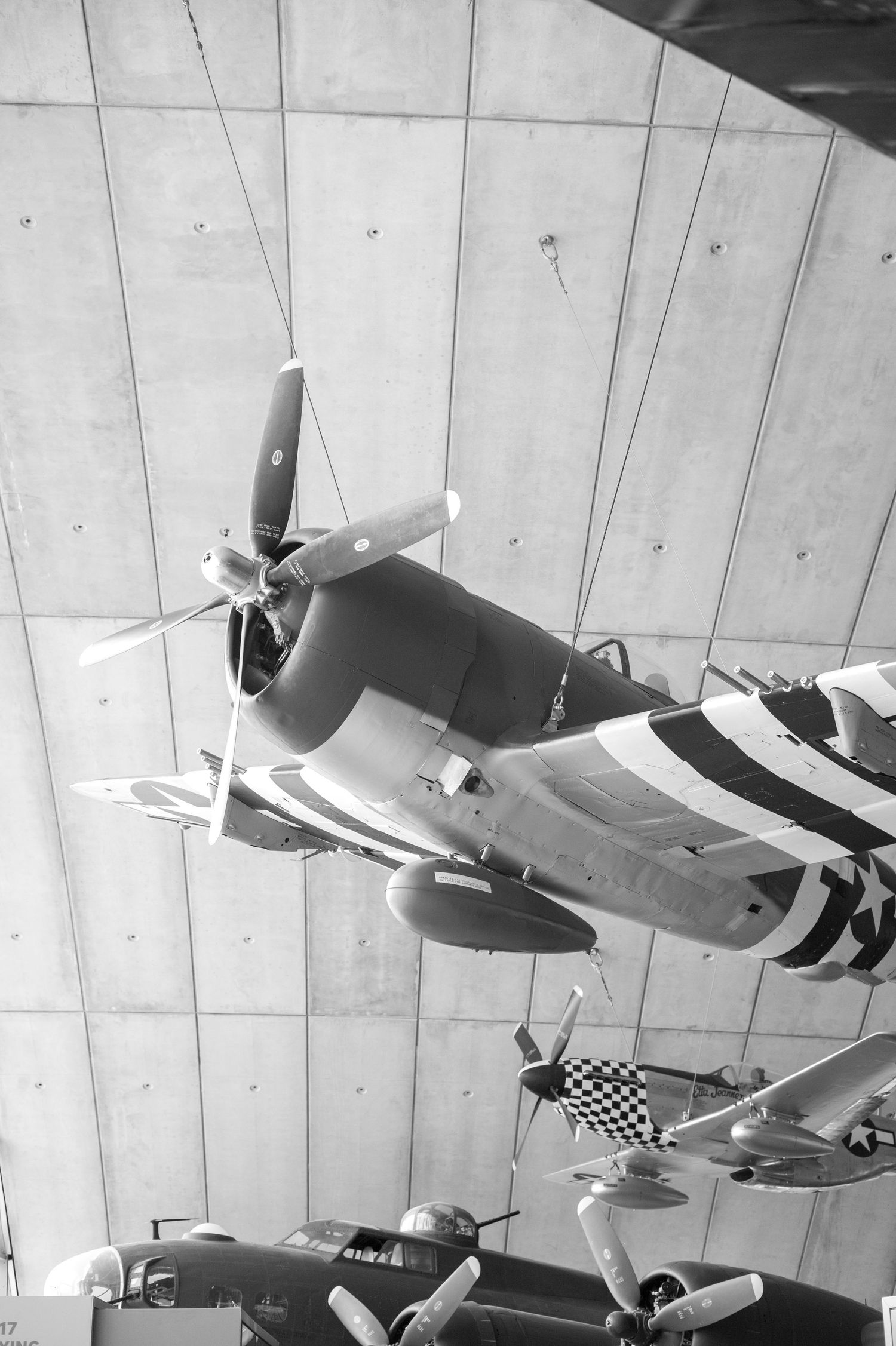Black and white photo of a WWII B-25 Mitchell bomber aircraft displayed in a museum, with nose art visible.