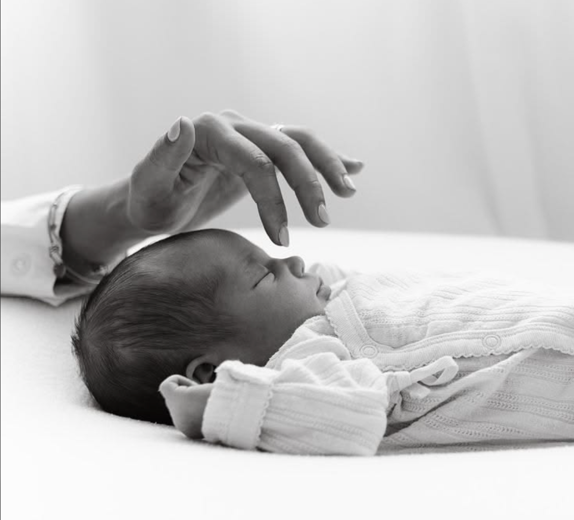 Pregnant woman in sheer gray draped fabric poses gracefully on reflective surface against dark background.