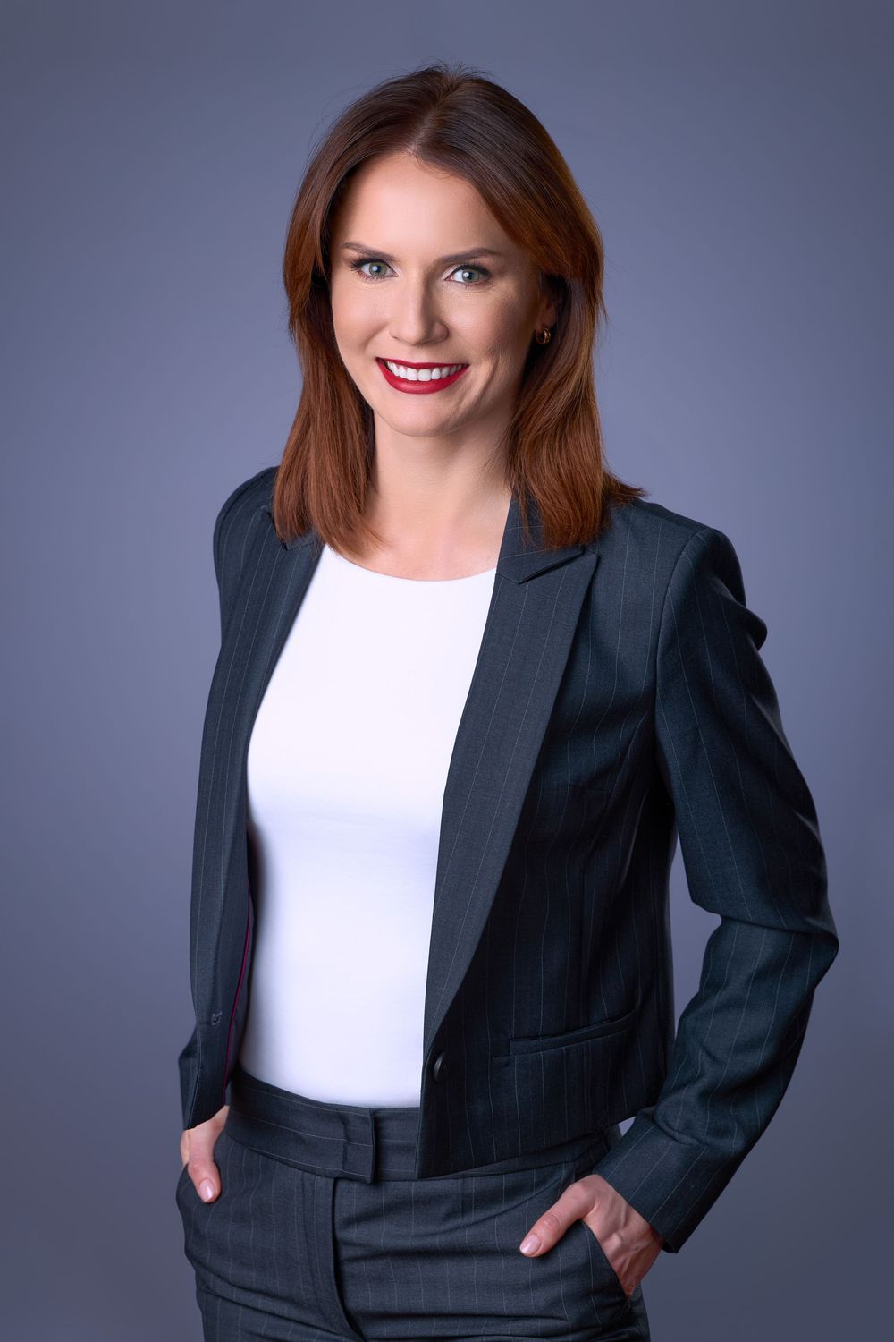 Professional businesswoman in gray suit and white blouse smiling confidently against a gray background.