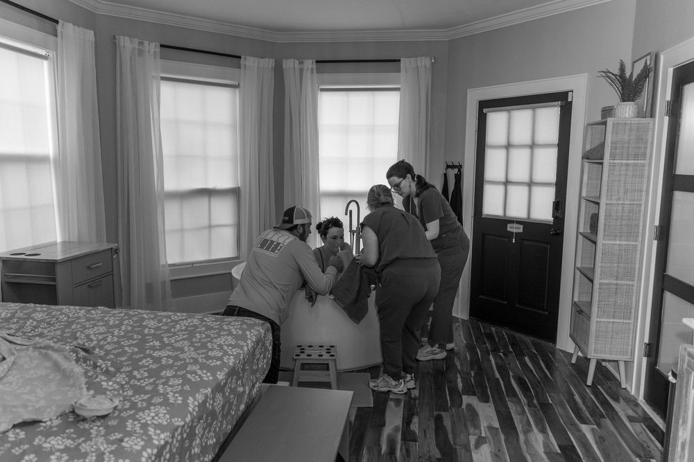 Group of people assembling furniture in a bright bedroom with hardwood floors and large bay windows.