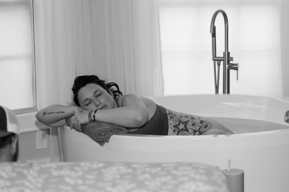 Black and white photo of tattooed woman resting in birthing tub during labor.