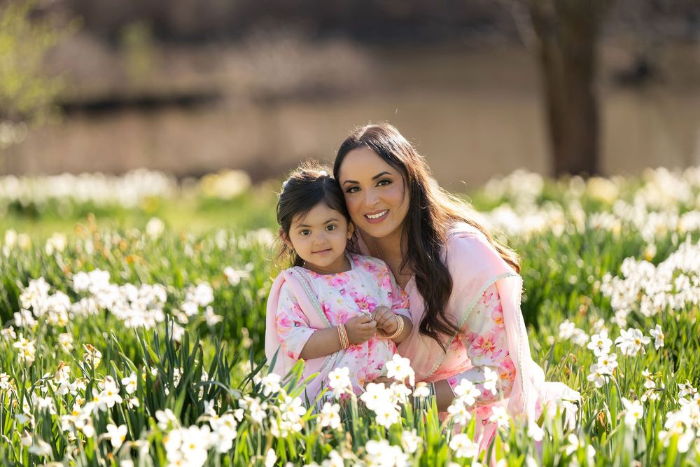 Mother and toddler daughter in coordinating pink floral outfits sitting in a daffodil garden.