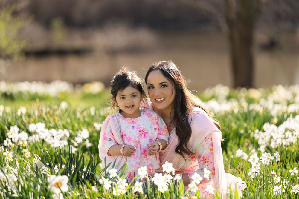 Cheerful mother and young daughter in pink outfits smiling together in a blooming daffodil field.