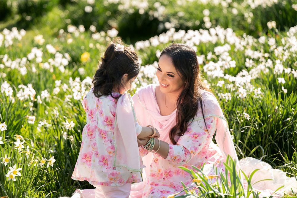 Mother and daughter in matching pink floral outfits sitting together in a field of white daffodils.