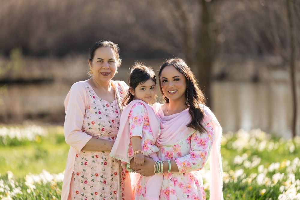 Grandmother, granddaughter, and mother in pink floral dresses posing in spring daffodil field.
