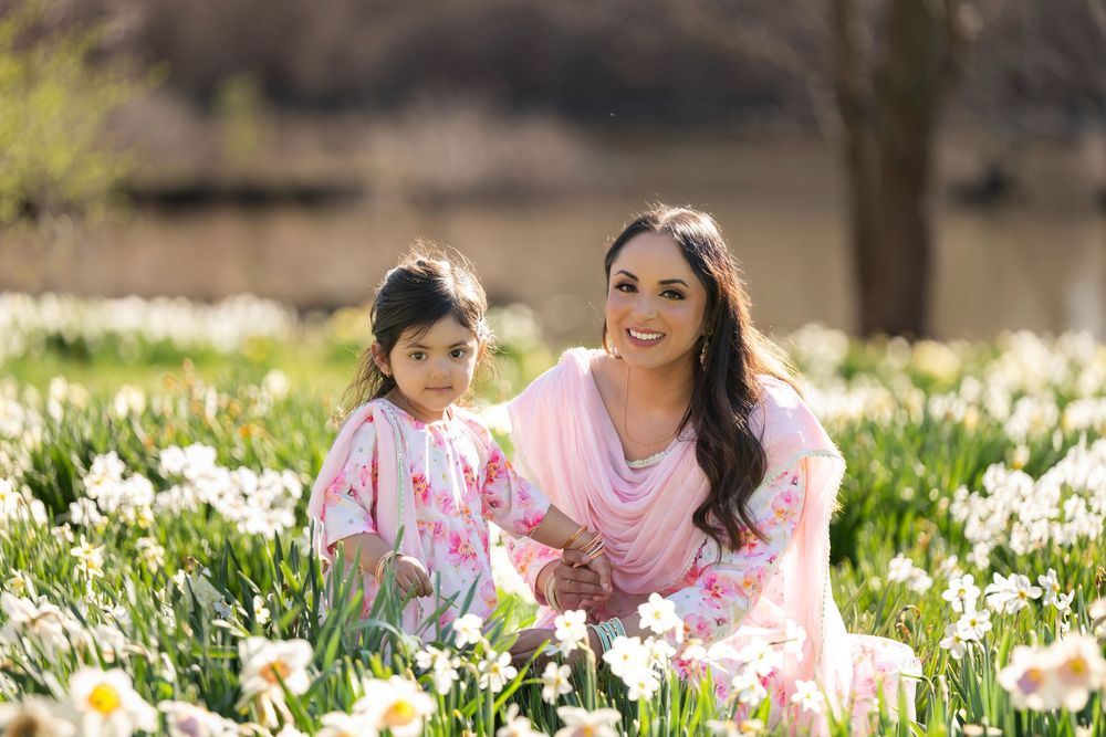 Mother and daughter in pink outfits sitting together among blooming white daffodils outdoors.