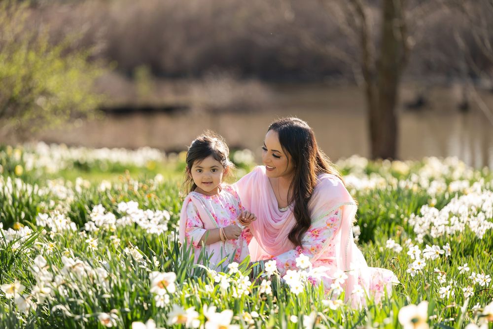 Woman in pink sari and little girl in floral dress sitting in a sunny daffodil meadow.