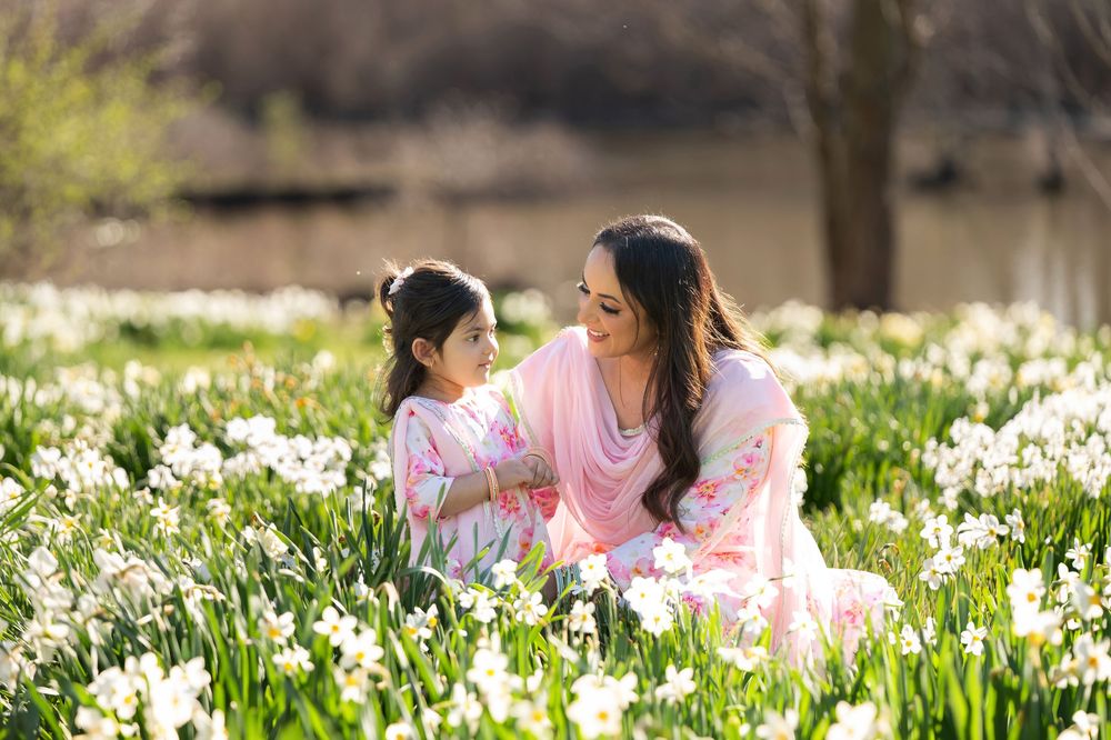 Mother and daughter in matching pink outfits gazing at each other in a white daffodil field.