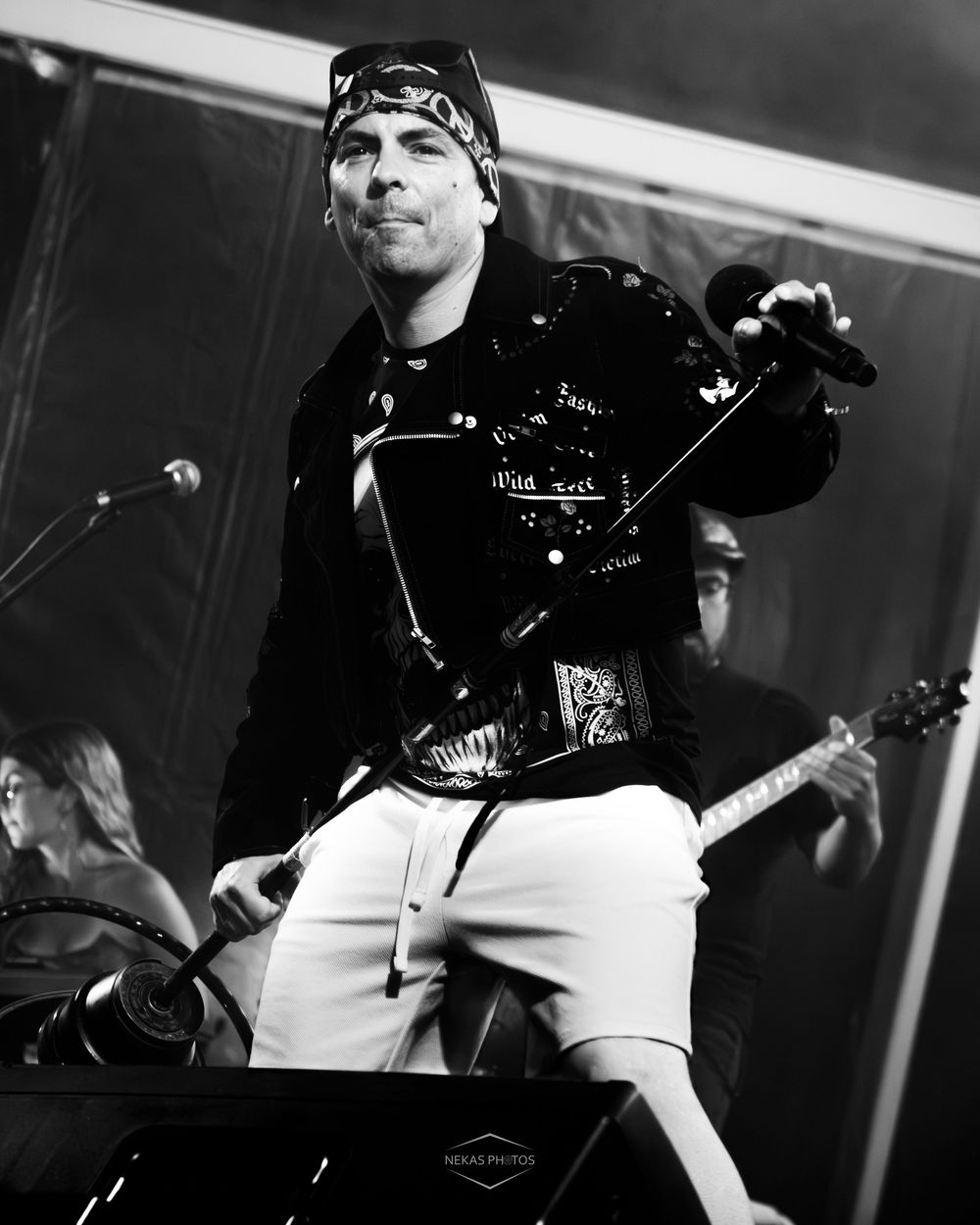 Black and white photo of a male rock performer singing on stage, wearing a bandana and leather jacket.