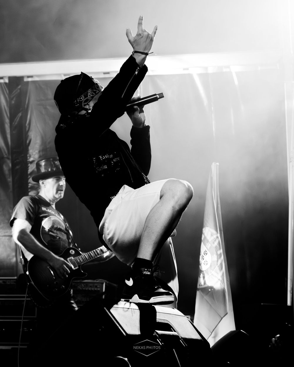 Black and white concert photo of a vocalist making a rock hand gesture while performing energetically on stage.