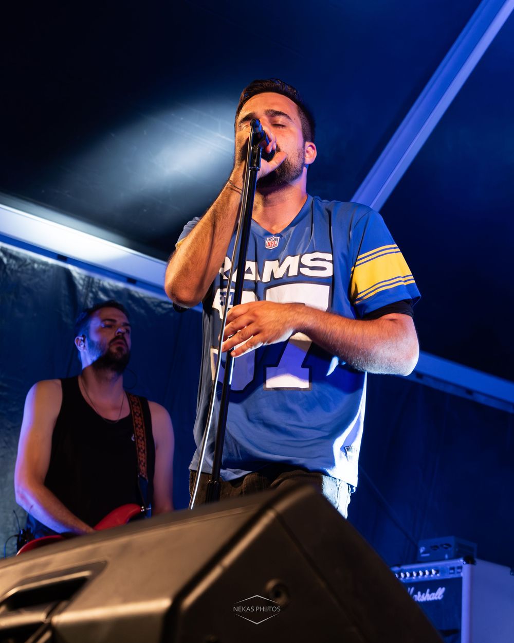 A male vocalist sings into a microphone wearing a Rams jersey at a live concert event.