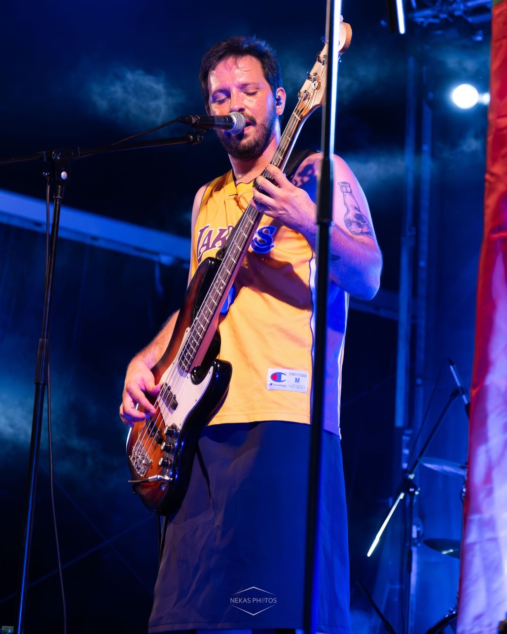 Male guitarist in yellow Lakers jersey performs on stage under blue lights at an outdoor concert.