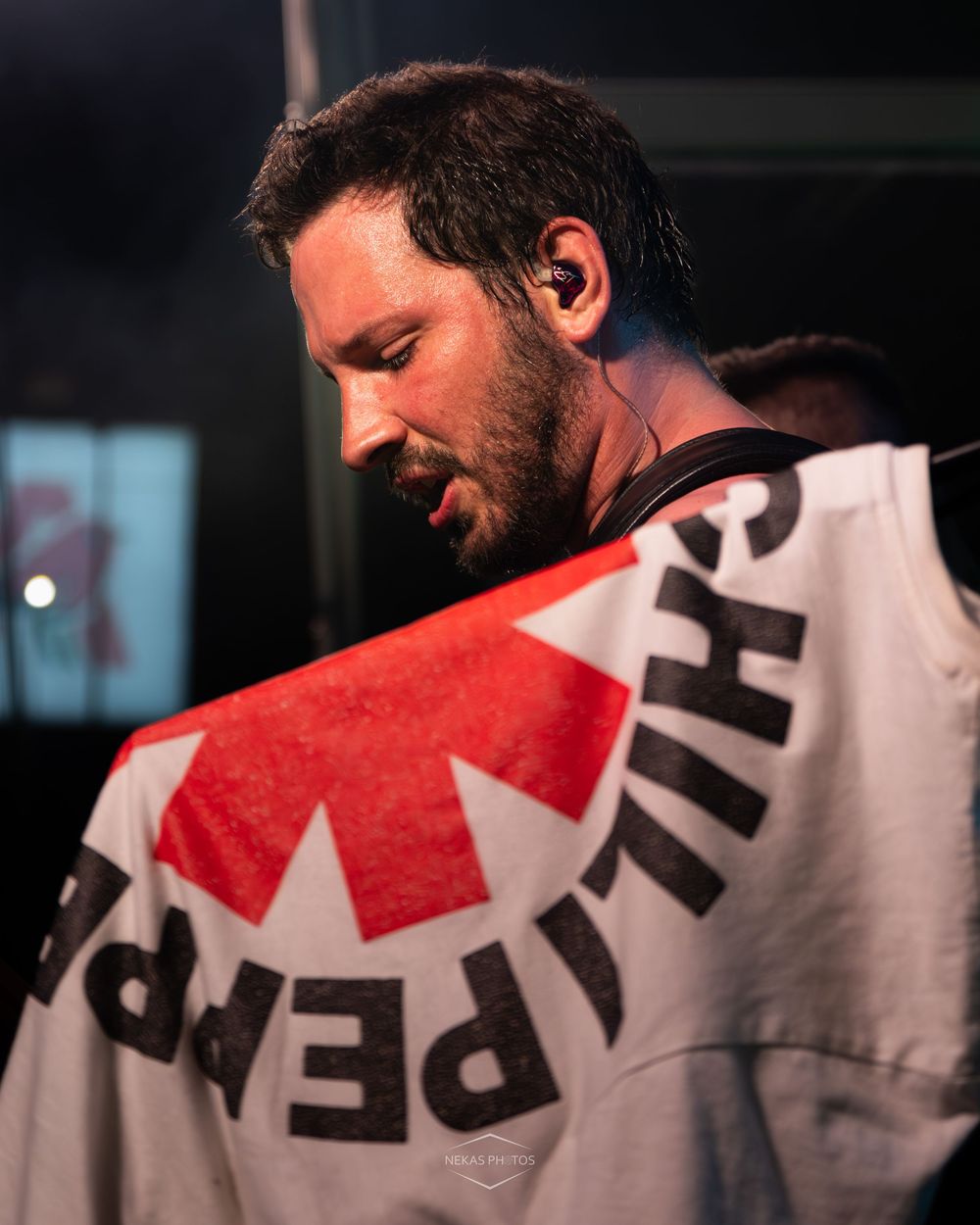 Bearded man with in-ear monitor holds a Red Hot Chili Peppers flag at a live music concert event.