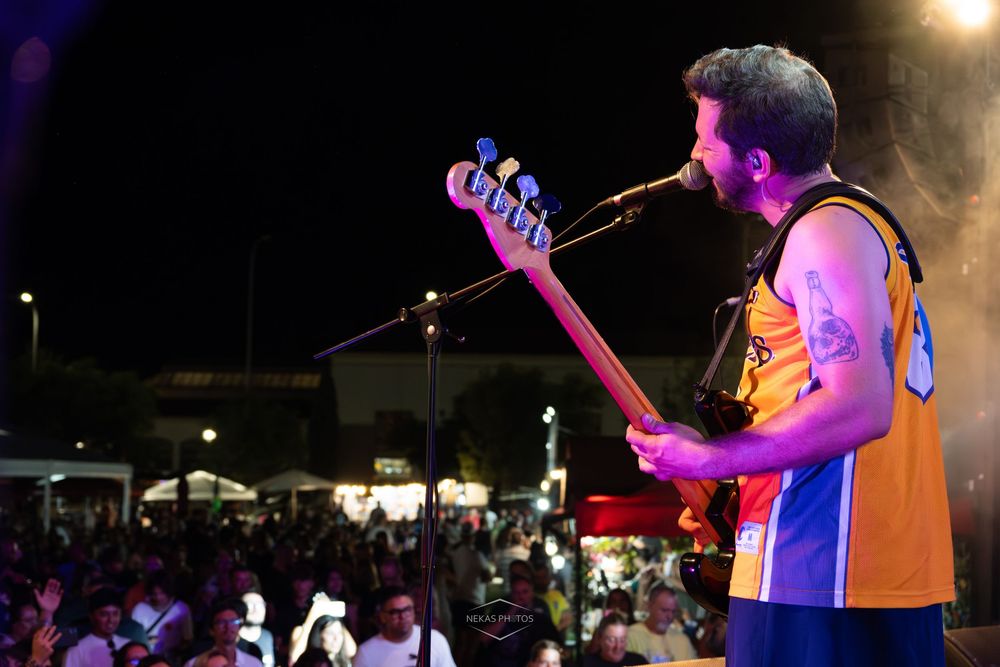 Guitarist performing on stage at an outdoor night concert, singing into a mic before a large crowd.