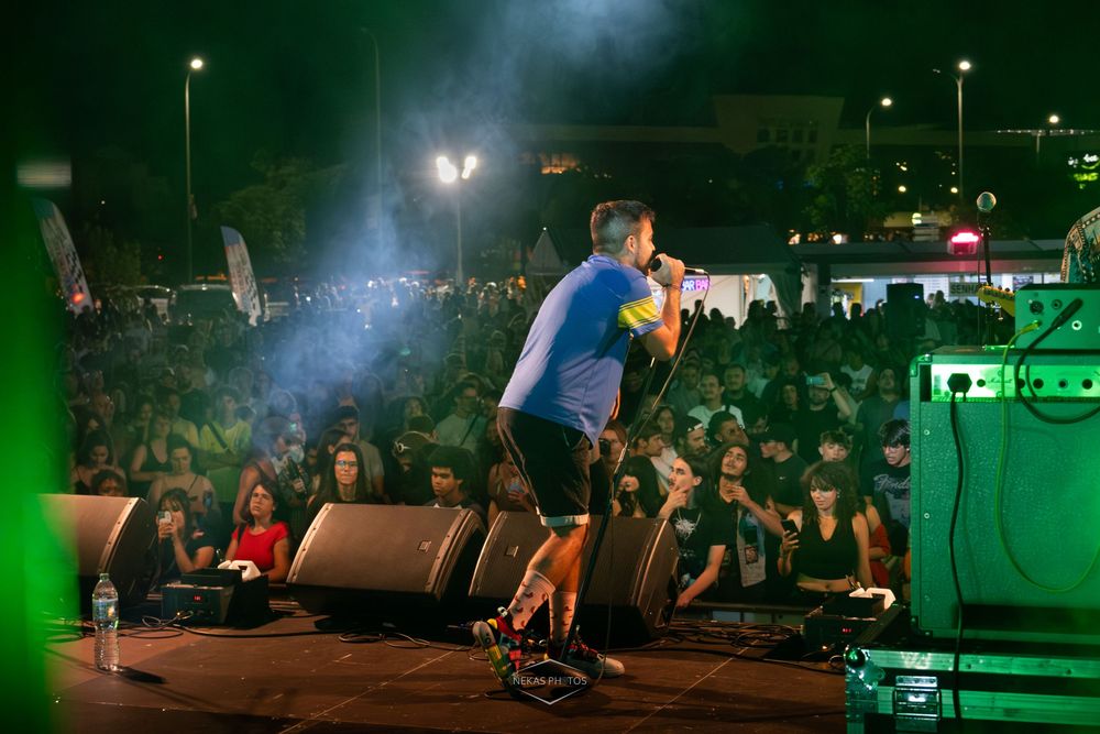 Performer on stage singing to a large crowd at an outdoor night concert with dramatic lighting and fog effects.