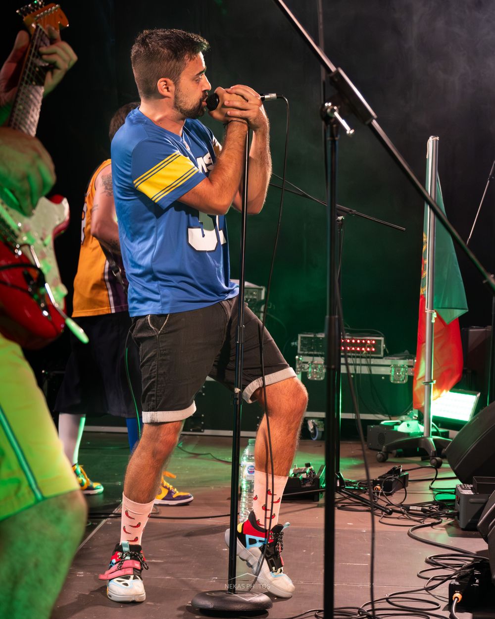 Male vocalist in blue jersey singing into microphone on stage during live concert performance.