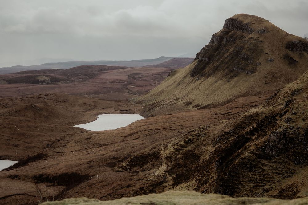 Dramatic Scottish Highland landscape featuring rugged brown hills, a small loch, and overcast skies at the Quiraing, Isle of Skye.